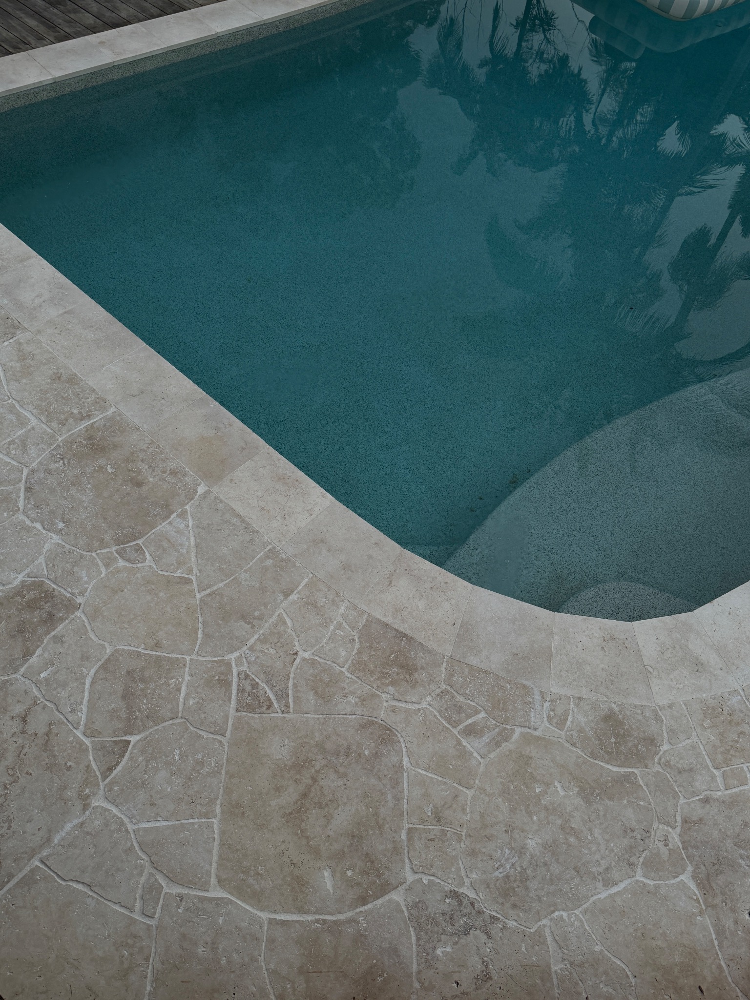Travertine crazy paving pool coping — natural stone finish detail.