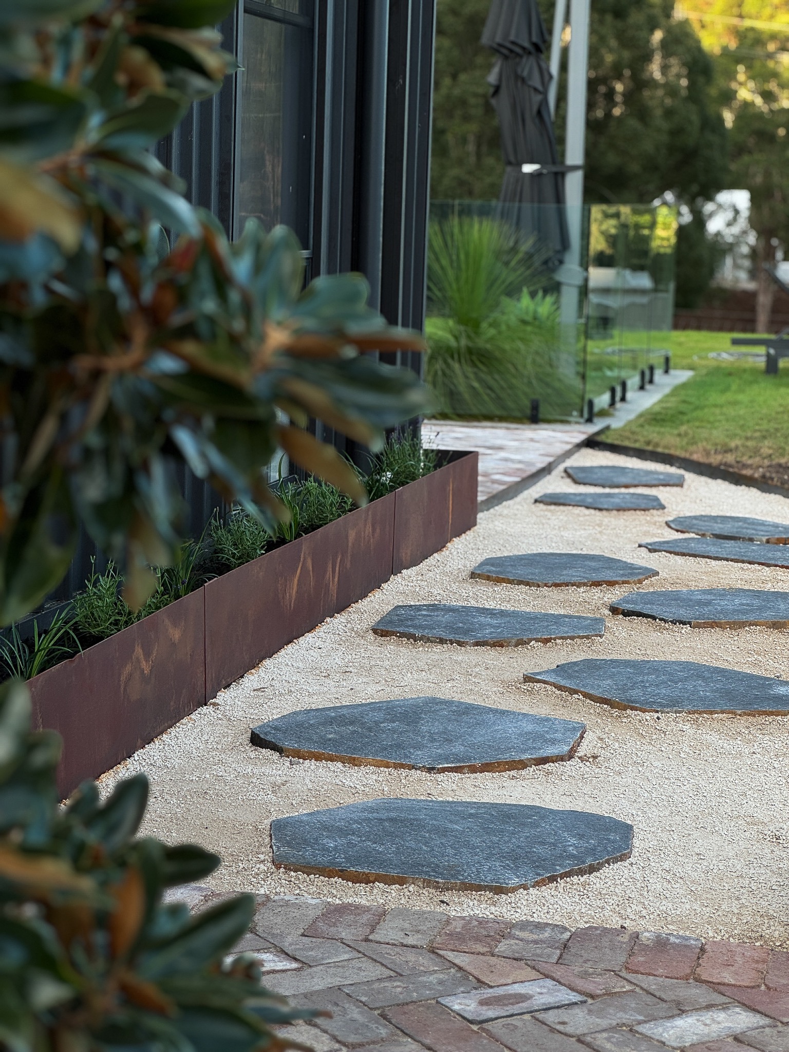 Slate stepping stone pathway with corten garden bed and glass fencing.